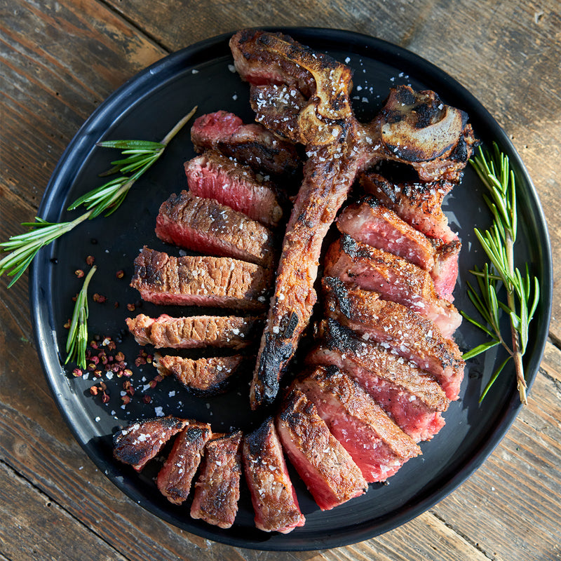Grilled steak on a black plate with rosemary on a wooden surface