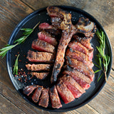Grilled steak on a black plate with rosemary on a wooden surface