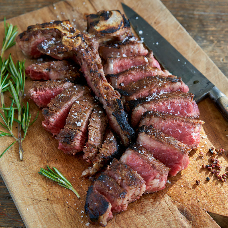 Sliced porterhouse steak on a wooden cutting board with rosemary and a knife.