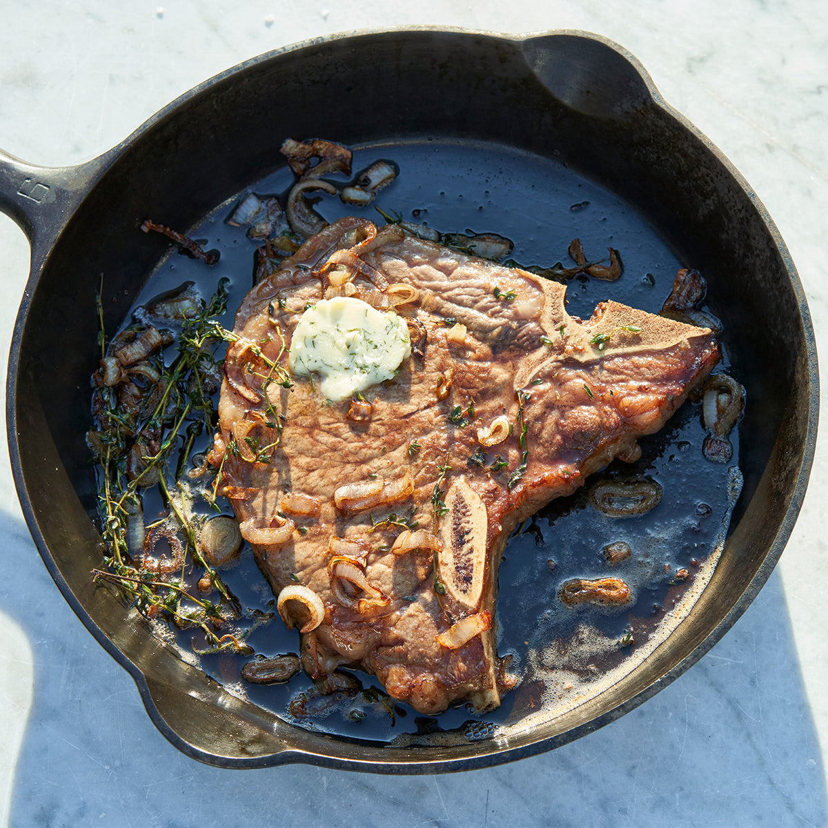 Steak with herb butter in a cast iron skillet on a light blue surface