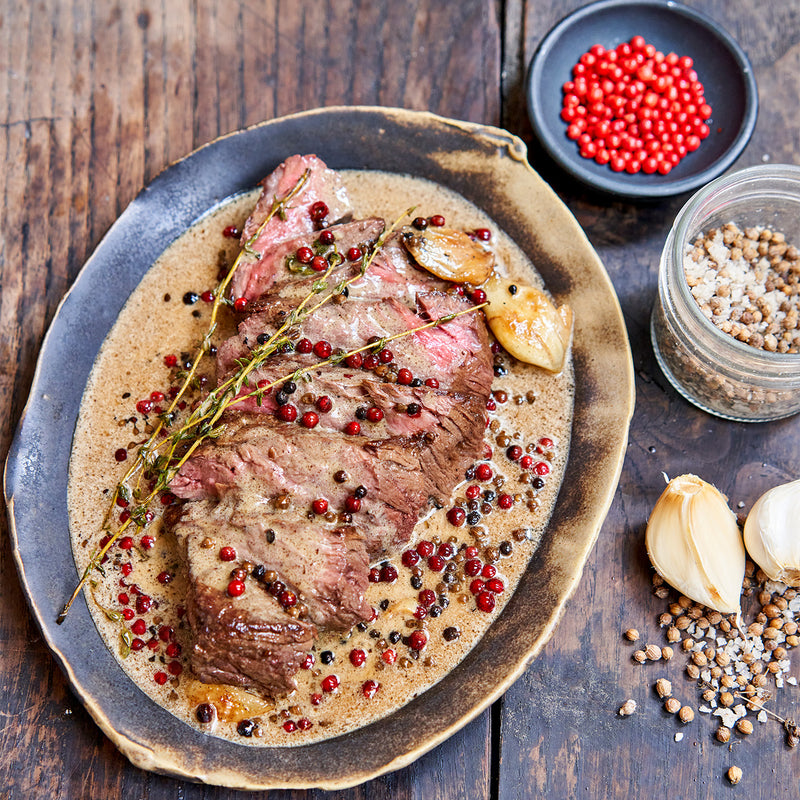 Roasted bavette steak with peppercorns on a wooden table