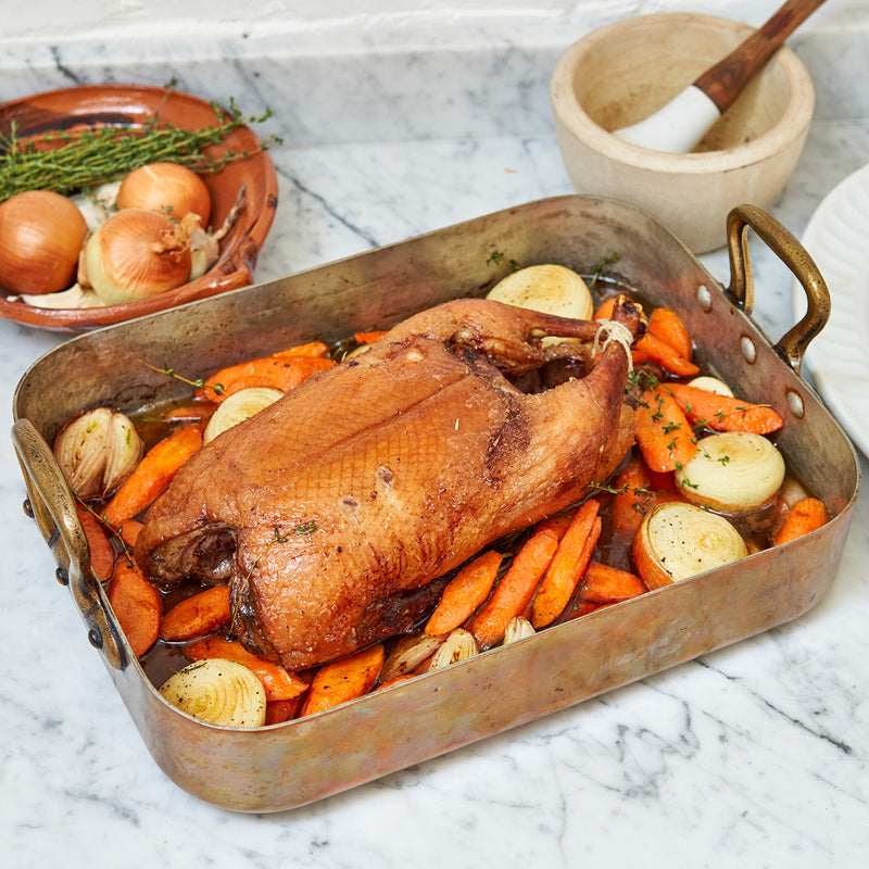 A whole cooked Moulard duck with carrot and onions in a casserole dish 