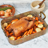 A whole cooked Moulard duck with carrot and onions in a casserole dish 