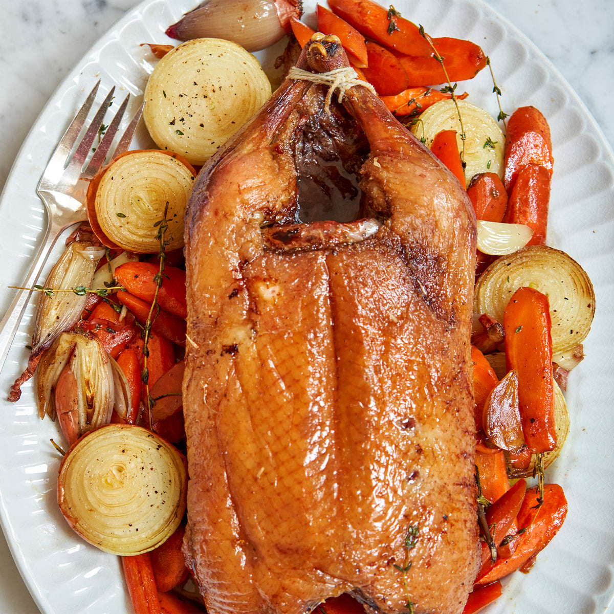 A whole cooked Moulard duck with carrot and onions in a casserole dish 