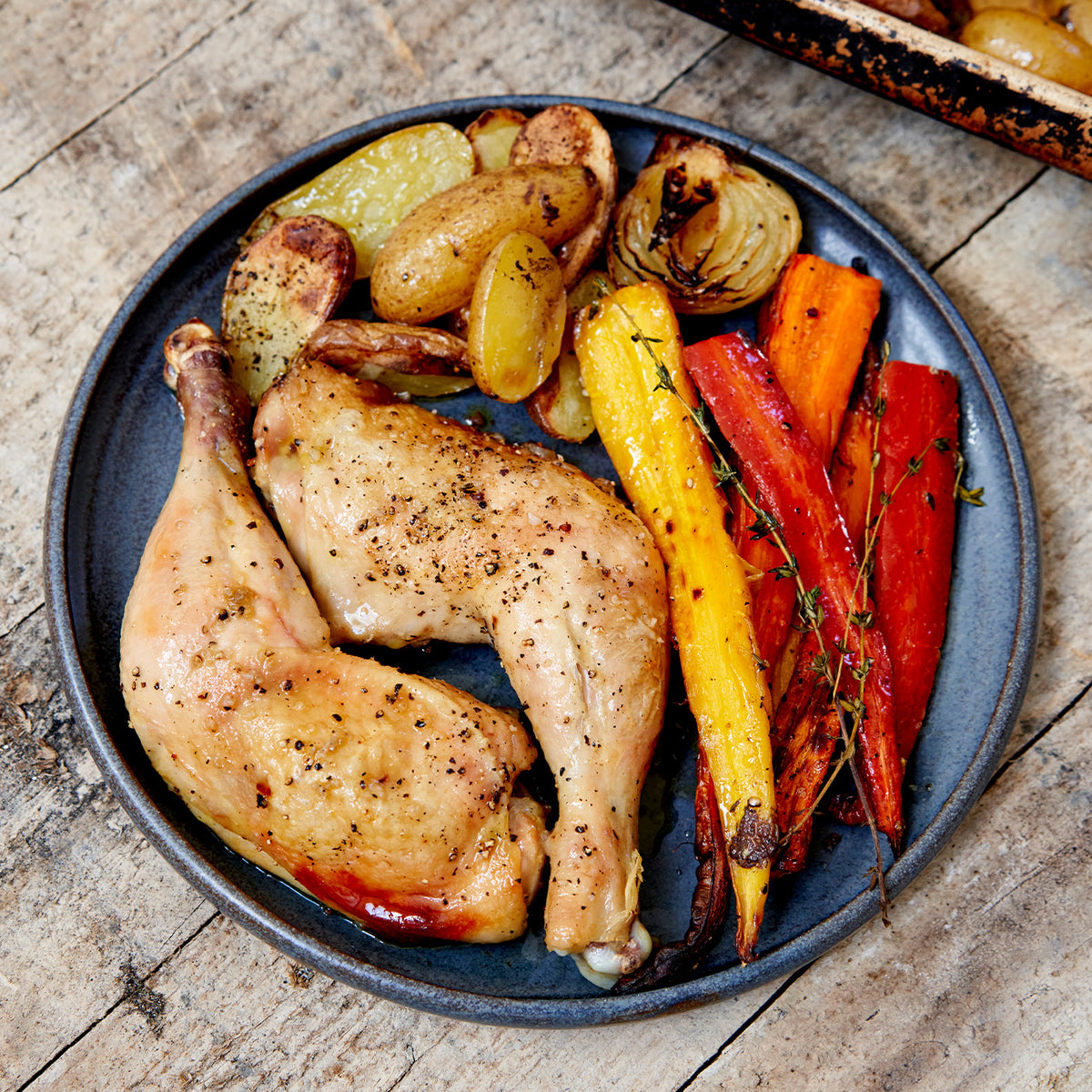 Plated cooked chicken legs with potatoes, onions, and roasted carrots. 