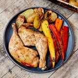 Plated cooked chicken legs with potatoes, onions, and roasted carrots. 