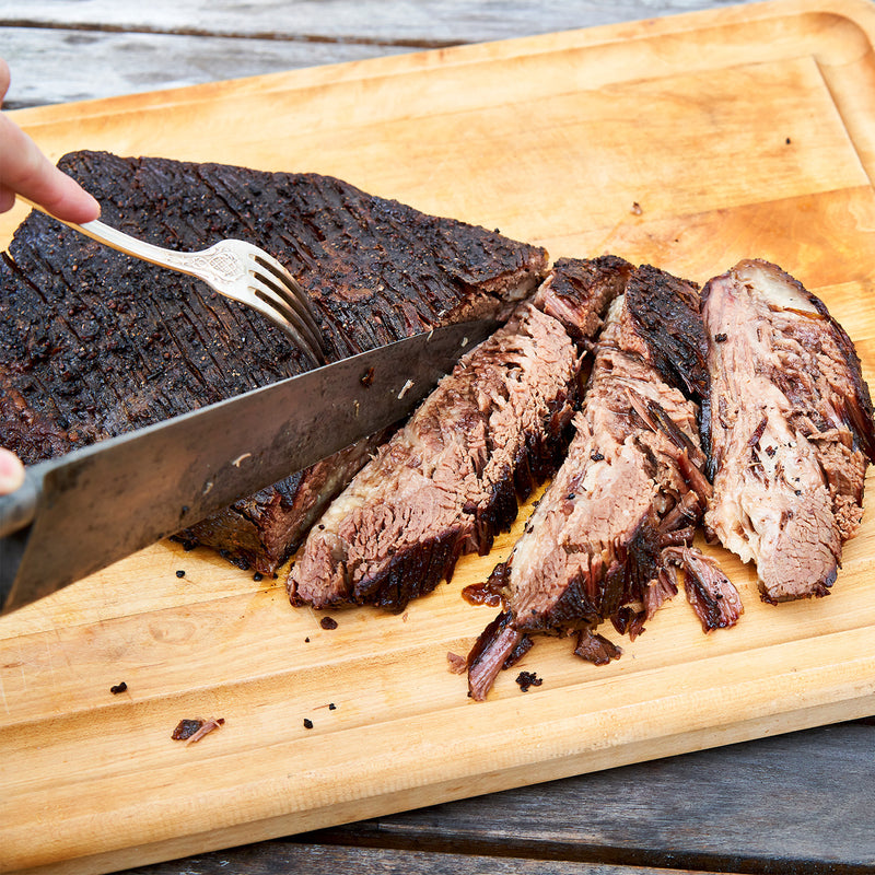 Sliced grilled steak on a wooden cutting board with a knife and fork.