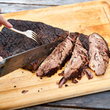 Sliced grilled steak on a wooden cutting board with a knife and fork.