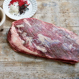 Raw flank steak on a wooden surface with seasonings in the background