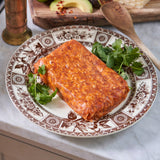 Marinated meat on a decorative plate with greens, on a kitchen counter.