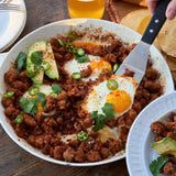  bowl of breakfast ground chorizo hash with eggs, avocado, and green onions on a wooden table.