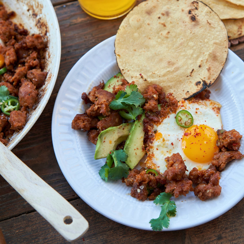Plate of breakfast tacos with ground meat, avocado, and an egg on a wooden table.