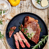Sliced steak on a black plate with herbs on a rustic wooden table