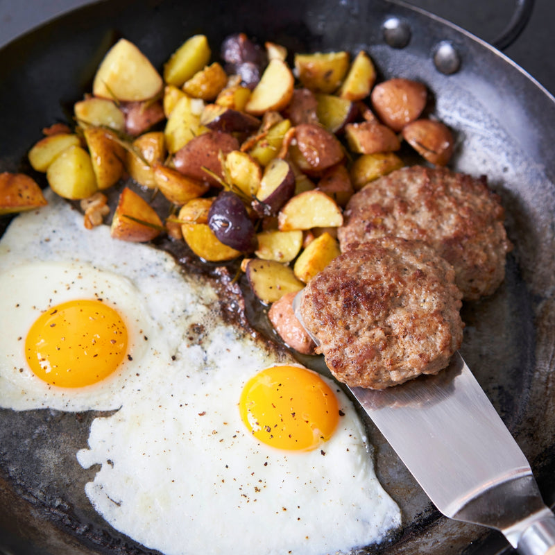 Fried eggs, sausage patties, and roasted potatoes in a skillet.