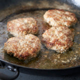 Four browned meat patties cooking in a frying pan.