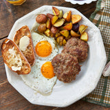 Plate of breakfast food including eggs, sausage, and potatoes on a wooden table.