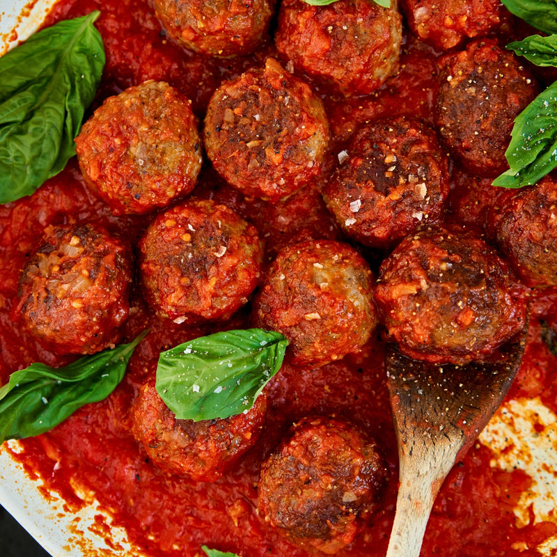 Meatballs in tomato sauce with basil leaves on a wooden spoon