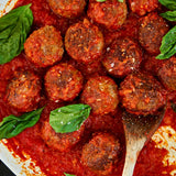 Meatballs in tomato sauce with basil leaves on a wooden spoon