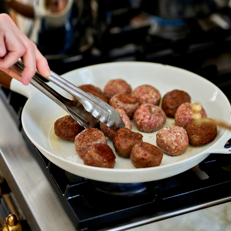 Person cooking meatballs in a pan on a stove