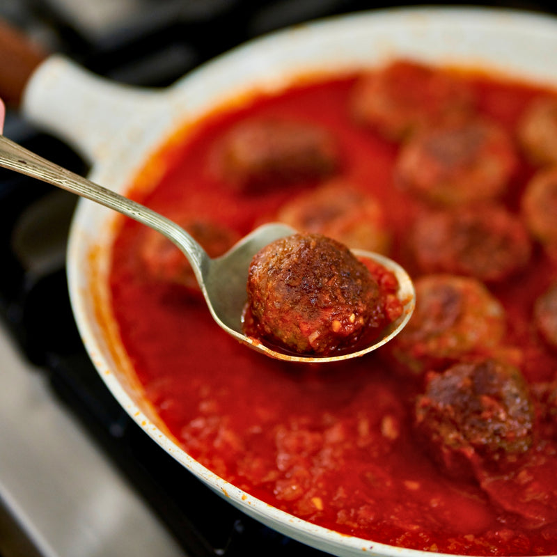 Spoon holding a meatball over a pan of meatballs in red sauce