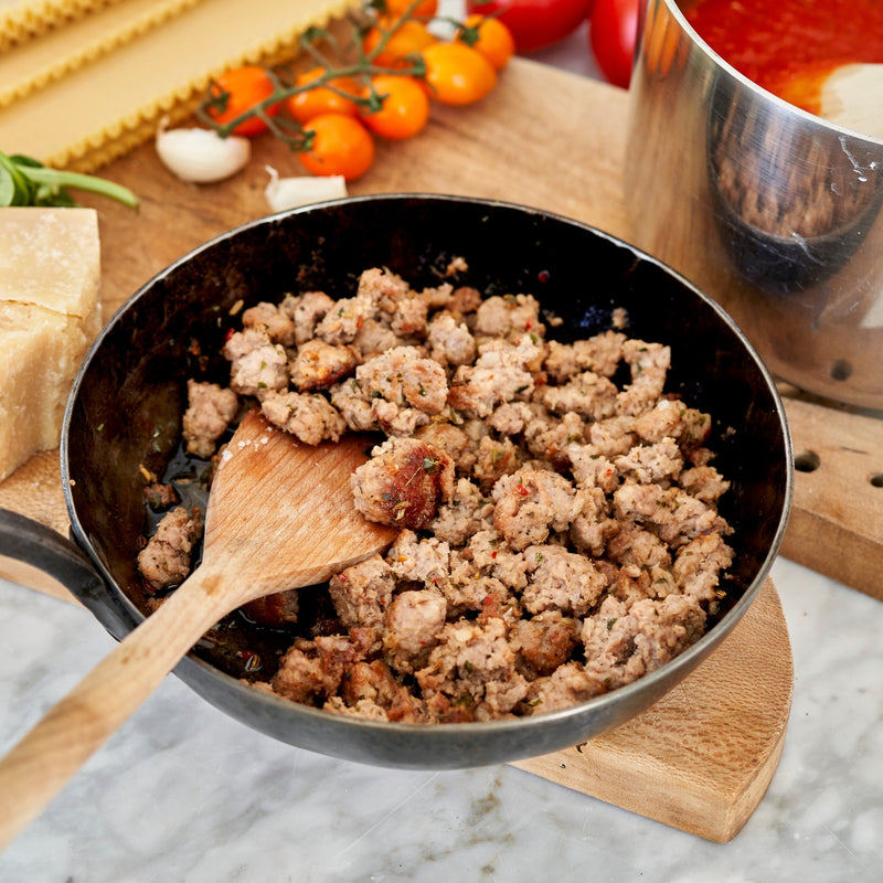Sautéed ground meat in a pan with a wooden spoon, surrounded by ingredients on a marble surface.