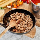 Sautéed ground meat in a pan with a wooden spoon, surrounded by ingredients on a marble surface.