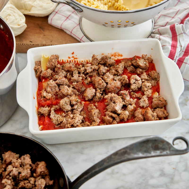Prepared dish with ground meat and tomato sauce in a white baking dish on a marble countertop.