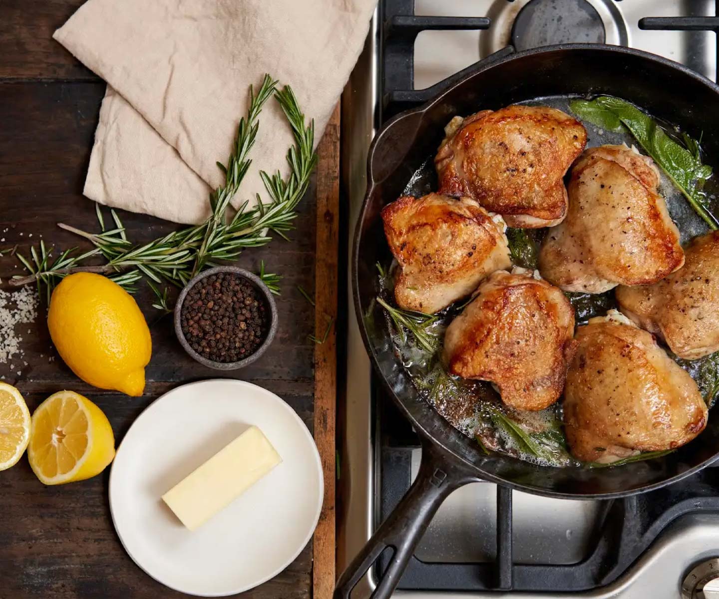 chicken thighs in a cast iron skillet surrounded by butter lemons and sage