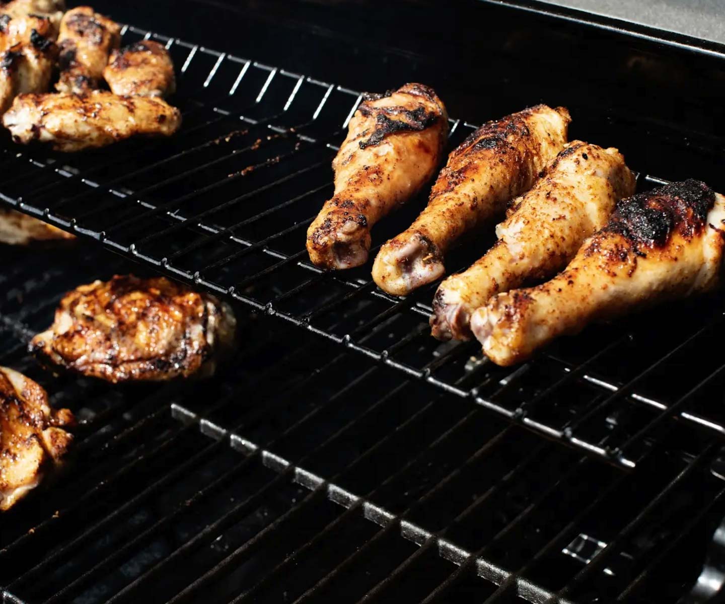 chicken drumsticks being cooked on the top rack of a grill