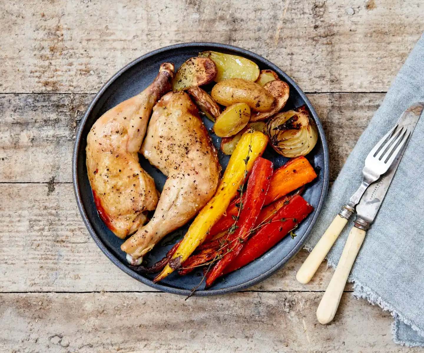 whole chicken legs on a plate with colorful carrots and potatoes